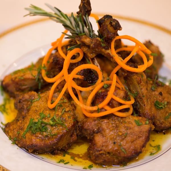 Indian lamb chops with rosemary and carrot garnish, served on a white plate with oil.