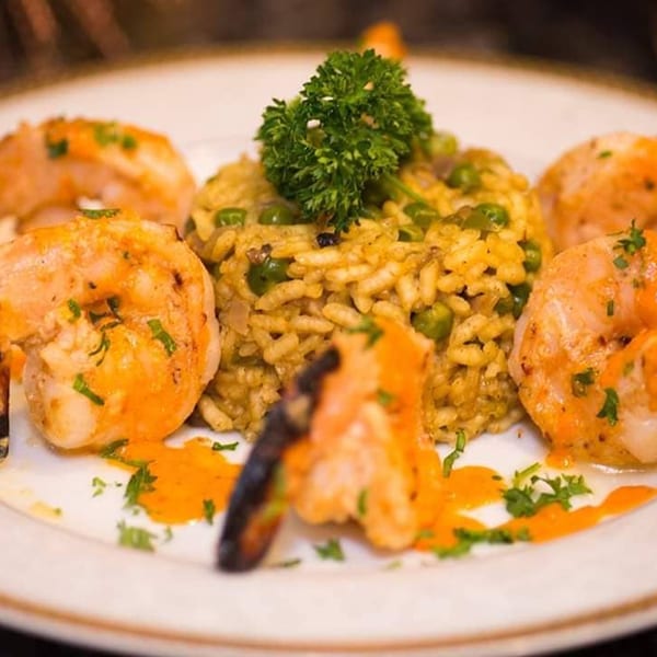 Narin's Bombay Brasserie's Indian shrimp dish with rice, peas, and parsley on a white plate.