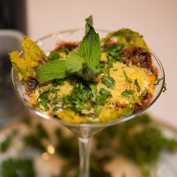 Indian chaat, garnished with mint and cilantro, served in a martini glass.