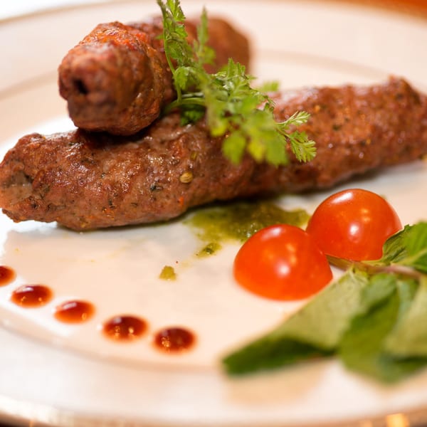 Two Narin's Bombay Brasserie seekh kebabs garnished with herbs, cherry tomatoes, and sauces.