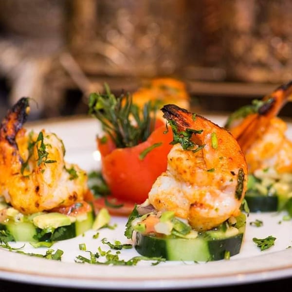 Grilled shrimp appetizers on cucumber slices with avocado and a tomato garnish at Narin's Bombay Brasserie.